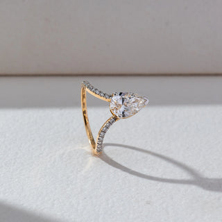 Side view of Pear Solitaire Diamond Ring in 14KT Yellow Gold, featuring a centred pear-shaped lab grown diamond with a pavé split band. Set on a beige backdrop, the design highlights structure and brilliance.
