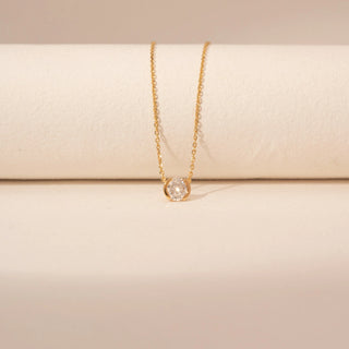Close-up view of a 14KT yellow gold necklace featuring a round-cut diamond pendant, set against a beige background.