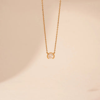 Front view of a 14KT yellow gold necklace featuring a round-cut diamond pendant, set against a beige background.