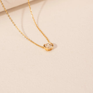 Angled view of a 14KT yellow gold necklace featuring a round-cut diamond pendant, set against a beige background.