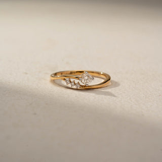 Front view of a bypass solitaire ring in 14 KT Yellow Gold, featuring a round lab-grown diamond accented by three smaller round diamonds along a flowing open-band design, displayed against a beige backdrop.