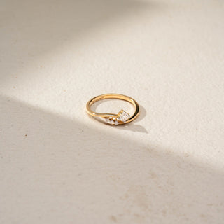 Top view of a bypass solitaire ring in 14 KT Yellow Gold, featuring a round lab-grown diamond accented by three smaller round diamonds along a flowing open-band design, displayed against a beige backdrop.
