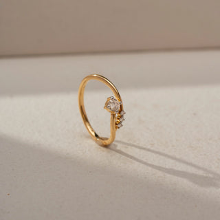 Angled view of a bypass solitaire ring in 14 KT Yellow Gold, featuring a round lab-grown diamond accented by three smaller round diamonds along a flowing open-band design, displayed against a beige backdrop.