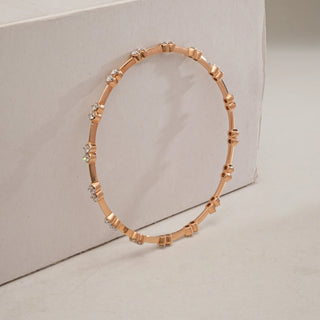 Rose Gold diamond bangle standing upright against a textured beige block, highlighting evenly spaced EF-VVS lab-grown diamonds along the slim circular frame.