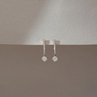Front view of diamond drop earrings in yellow gold, featuring vertical rows of round lab-grown diamonds with a square-cut diamond drop at the base. Set against a dual-tone neutral backdrop, they reflect clean elegance.