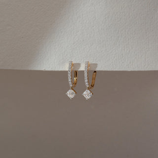 Side view of diamond hoop drop earrings in yellow gold, featuring round lab-grown diamonds along the hoop with a square-cut diamond drop. Set against a dual-tone neutral backdrop, they reflect clean elegance.