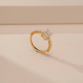 Angled view of a 14KT Yellow Gold diamond ring, featuring a rectangular step-cut centre diamond and diamond-set shoulders.