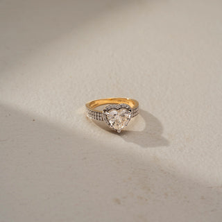Top view of a heart halo engagement ring in White Gold, featuring a heart-shaped lab-grown diamond encircled by a sparkling halo and set on a triple-row pavé diamond band, displayed against a beige backdrop.
