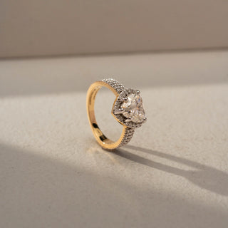Side view of a heart halo engagement ring in White Gold, featuring a heart-shaped lab-grown diamond encircled by a sparkling halo and set on a triple-row pavé diamond band, displayed against a beige backdrop.