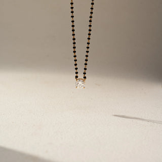 Front view of a yellow gold lab-grown diamond mangalsutra featuring a round solitaire diamond pendant on a classic black bead chain, displayed on a neutral background.