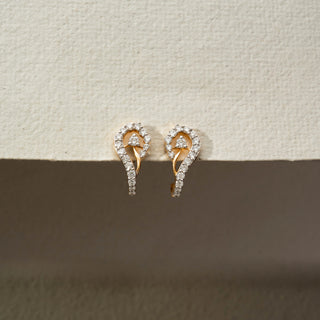 Front view of diamond swirl stud earrings in 14KT Yellow Gold, featuring pavé-set lab-grown diamonds in a flowing teardrop design. Captured against a beige backdrop, highlighting elegance and brilliance.