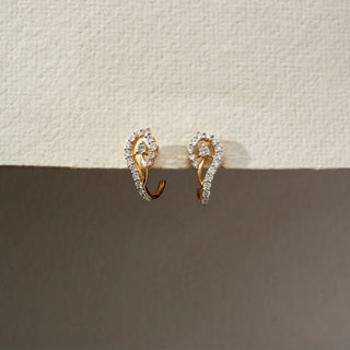 Angled side view of diamond swirl hoop earrings in 14KT Yellow Gold, featuring pavé-set lab-grown diamonds in an open teardrop design. Captured against a beige backdrop, highlighting fluid elegance.