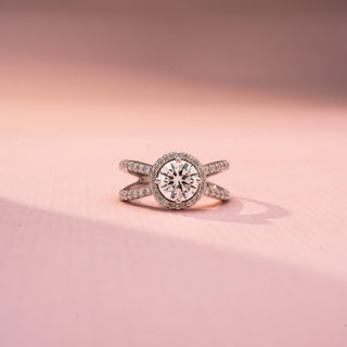Front view of a round halo engagement ring in White Gold, featuring a round lab-grown diamond encircled by a sparkling halo and set on a split pavé diamond band, displayed against a soft pink backdrop.