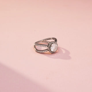 Side view of a round halo engagement ring in White Gold, featuring a round lab-grown diamond encircled by a sparkling halo and set on a split pavé diamond band, displayed against a soft pink backdrop.