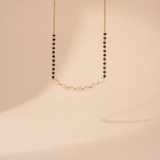 Front view of a 14KT yellow gold mangalsutra featuring alternating oval, pear and emerald-cut diamonds with black beads, set against a beige background.
