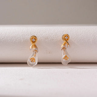 Front view of gold drop earrings, featuring twisted diamond accents with translucent teardrop danglers. Captured against a soft beige backdrop, the design reflects delicate elegance and modern charm.

