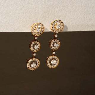 Angle view of diamond floral drop earrings in 14 KT Yellow Gold, featuring three cascading flower-inspired diamond clusters with scalloped halos against a neutral backdrop.
