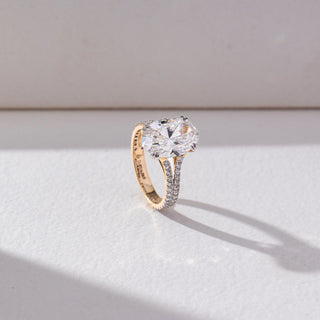 Side view of Oval Solitaire Diamond Ring in 14KT Yellow Gold, featuring a centred oval lab grown diamond with a double pavé-set band. Set on a beige backdrop, the design highlights depth and brilliance.
