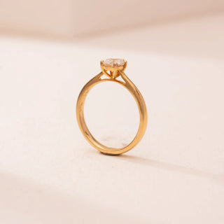 Side view of Reia’s 14 KT Yellow Gold Classic Pear Diamond Promise Ring. A pear-shaped lab-grown diamond solitaire is set on a polished gold band against a soft pink surface.