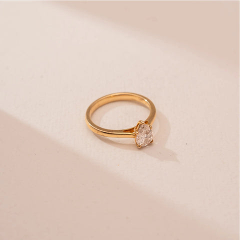 Top view of Reia’s 14 KT Yellow Gold Classic Pear Diamond Promise Ring. A pear-shaped lab-grown diamond solitaire is set on a polished gold band against a soft pink surface.