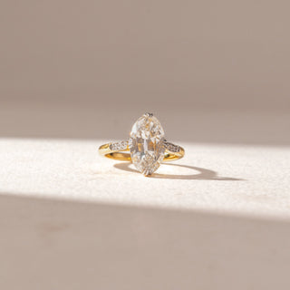 Front view of Marquise Diamond Solitaire Ring in 14KT Yellow Gold, featuring a large marquise-cut center diamond with pavé side accents. Set on a soft beige surface, the design reflects timeless elegance and sparkle.
