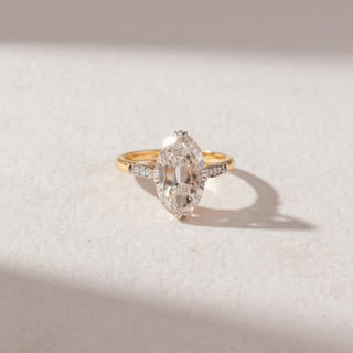 Top view of Marquise Diamond Solitaire Ring in 14KT Yellow Gold, featuring a large marquise-cut center diamond with pavé side accents. Set on a soft beige surface, the design reflects timeless elegance and sparkle.
