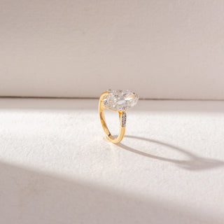 Angled side view of Marquise Diamond Solitaire Ring in 14KT Yellow Gold, featuring a large marquise-cut center diamond with pavé side accents. Set on a beige surface, it reflects refined elegance and sparkle.
