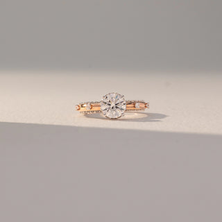 Front view of Round Solitaire Diamond Ring in 14KT Rose Gold, featuring a centred round lab grown diamond with channel-set side accents. Set on a beige backdrop, the design highlights classic elegance and sparkle.
