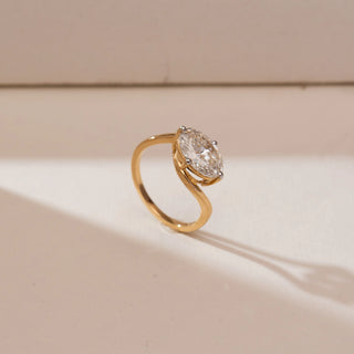 Angled side view of Horizontal Oval Bypass Diamond Ring in yellow gold, showcasing a horizontally set oval lab-grown diamond embraced by a flowing bypass band, displayed on a soft beige backdrop.