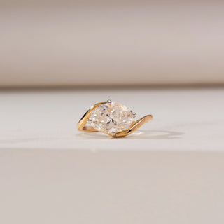 Front view of Horizontal Oval Bypass Diamond Ring in yellow gold, featuring a horizontally set oval lab-grown diamond embraced by a flowing bypass band, displayed on a soft beige surface.