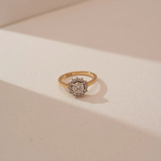 Angled top view of Reia’s 14 KT Yellow Gold Classic Aura Diamond Halo Ring. Captured against a cream backdrop, the layout highlights the luminous round brilliant-cut diamond and delicate halo.