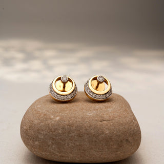 Front view of circular diamond stud earrings in 14 KT Yellow Gold, featuring pavé-set crescent accents with bezel-set round diamonds, displayed on a textured stone surface.
