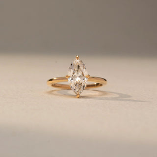 Front view of a marquise solitaire engagement ring in 14 KT Yellow Gold, featuring a marquise-cut lab-grown diamond in a classic six-prong setting, displayed against a beige backdrop.