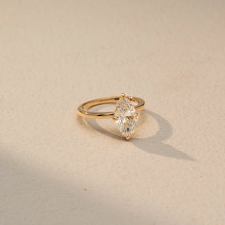 Side view of a marquise solitaire engagement ring in 14 KT Yellow Gold, featuring a marquise-cut lab-grown diamond in a classic six-prong setting, displayed against a beige backdrop.