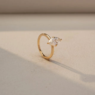 Angled view of a marquise solitaire engagement ring in 14 KT Yellow Gold, featuring a marquise-cut lab-grown diamond in a classic six-prong setting, displayed against a beige backdrop.