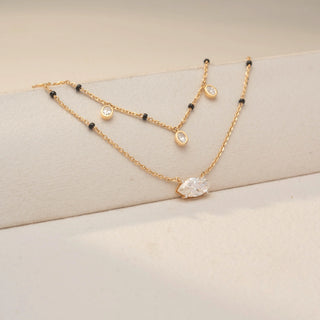 Side view of two Diamond Mangalsutra designs in 14KT Yellow Gold — one featuring bezel-set oval diamond drops on a black bead chain, and another with a bold marquise solitaire pendant. Captured against a beige backdrop.