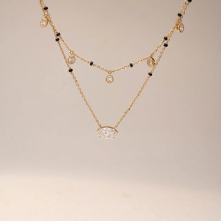Front view of two Diamond Mangalsutra designs in 14KT Yellow Gold — one featuring bezel-set oval diamond drops on a black bead chain, and another with a bold marquise solitaire pendant. Captured against a beige backdrop.
