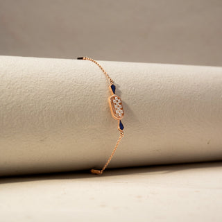 Side  view of a diamond bracelet in 14 KT Rose Gold, featuring an oval diamond cluster centerpiece accented with deep blue geometric gemstones on a delicate chain, displayed against a soft beige backdrop.
