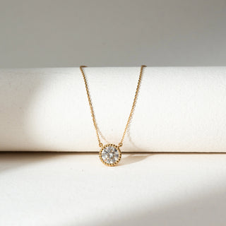 Front view of Round Bezel Diamond Pendant Necklace in 14KT Yellow Gold, featuring a centred round lab grown diamond in a textured bezel setting. Placed on a beige backdrop, the design highlights minimal elegance and refined sparkle.
