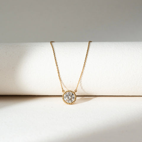Front view of Round Bezel Diamond Pendant Necklace in 14KT Yellow Gold, featuring a centred round lab grown diamond in a textured bezel setting. Placed on a beige backdrop, the design highlights minimal elegance and refined sparkle.
