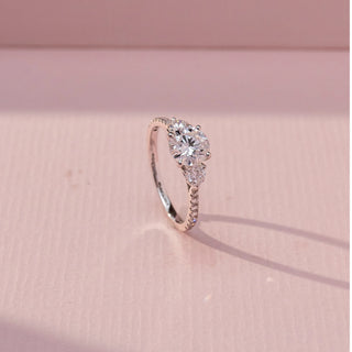 Side view of Round Three Stone Diamond Ring in 14KT White Gold, featuring a centred round lab grown diamond with round side stones and pavé band. Set on a pink backdrop, the design highlights depth and elegance.
