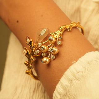 Nature-inspired gold cuff bracelet with sculpted branch and leaf details, accented by pearl drops and small diamonds for a bold and artistic statement design.