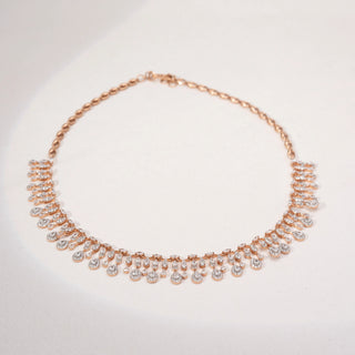 Top view of a teardrop lab-grown diamond necklace in 14KT Rose Gold, featuring cascading bezel-set diamond drops in a graceful fringe design. Captured against a beige backdrop, the elegant silhouette radiates brilliance.
