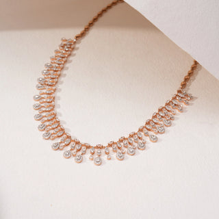 Angled view of a teardrop lab-grown diamond necklace in 14KT Rose Gold, featuring cascading pear-shaped diamond drops in an elegant fringe design. Captured against a beige backdrop, the graceful silhouette radiates brilliance.