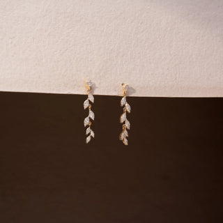Angled view of diamond drop earrings in 14 KT Yellow Gold, featuring cascading marquise-shaped diamond motifs suspended from delicate diamond studs against a neutral backdrop.
