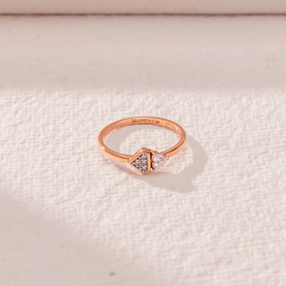 Top view of geometric diamond ring in rose gold, featuring a round lab-grown diamond paired with a triangle-shaped cluster. Placed on a textured beige surface, the design casts a soft shadow.
