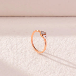 Side view of geometric diamond ring in rose gold, featuring a round lab-grown diamond paired with a triangle-shaped cluster. Set on a textured beige surface, the design casts a soft elongated shadow.
