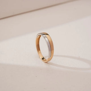 Angled view of Sleek Flush Set Diamond Band in dual gold, showcasing a single round lab-grown diamond set flush within a smooth yellow and white gold band against a neutral backdrop.