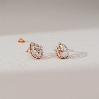 Angled view of floral diamond drop earrings in rose gold, featuring round lab-grown diamonds in a blooming cluster within a teardrop frame lined with diamonds. Set on a soft neutral surface, they highlight delicate sparkle.