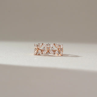 Front view of floral diamond band ring in rose gold, featuring marquise-shaped lab-grown diamonds forming intricate flower motifs. Captured against a soft beige background with gentle shadows.